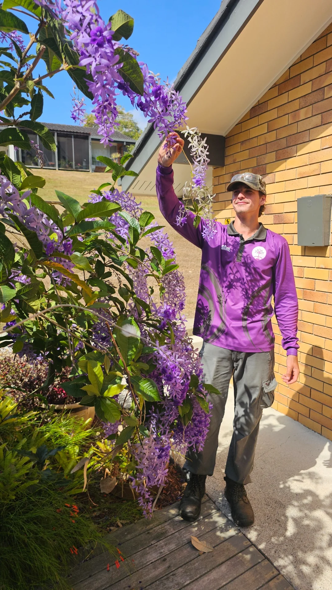 An Excel team member examining cascading purple flowers beside a village home