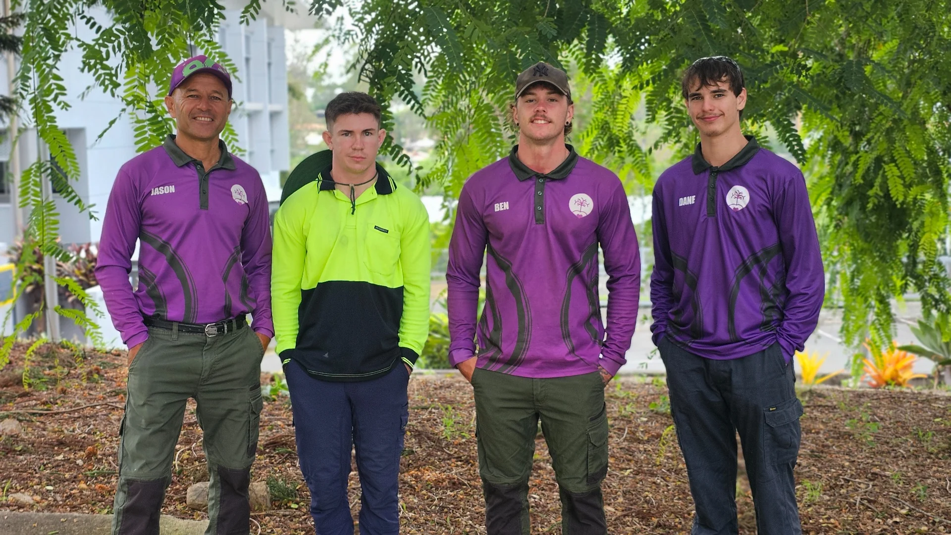 Four team members standing together beneath leafy trees in the village grounds